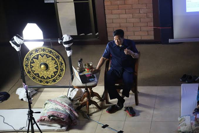 Master Mantak Chia teaching students in the dark room while sitting next to a golden gong