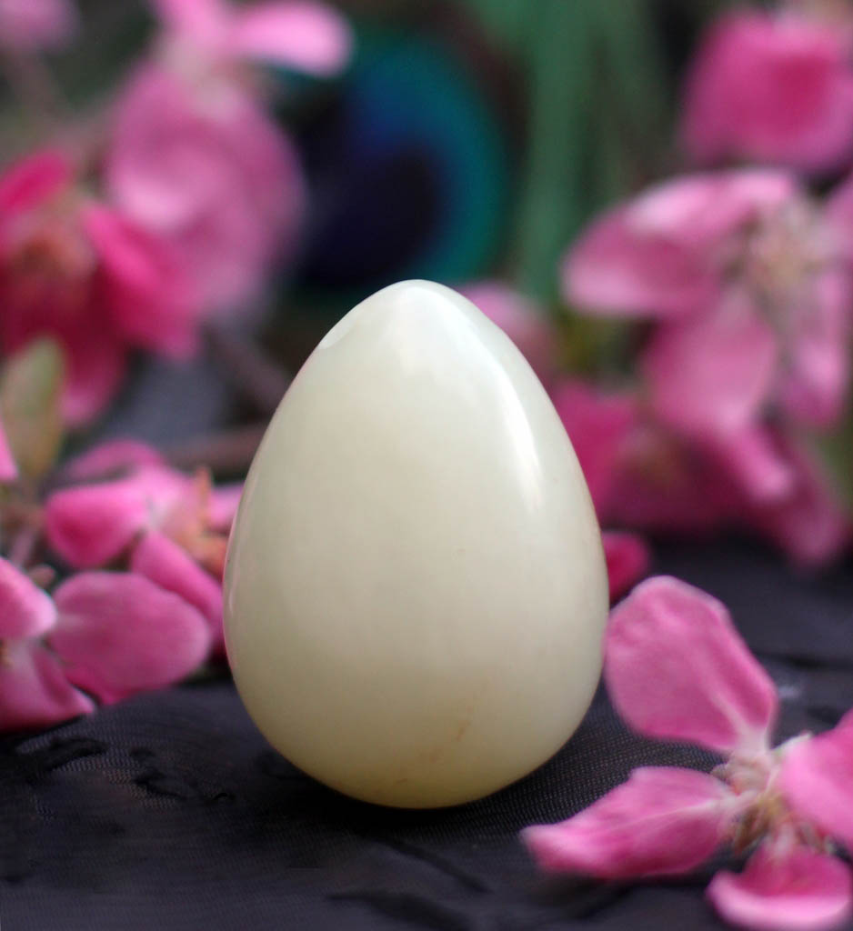 Healing Tao Australia yoni egg which is made from white nephrite jade and has pink flowers in the background